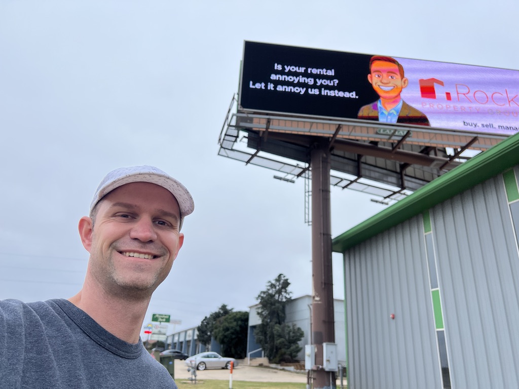 A selfie in front of a Rock Property Group digital billboard reading: Is your rental annoying you? Let it annoy us instead.